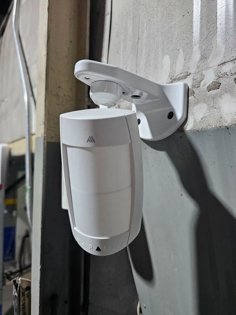 Detector de movimiento PARADOX instalado en pared con soporte articulado